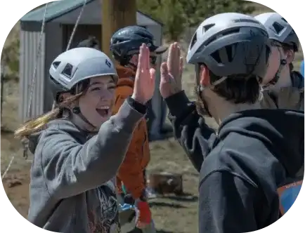 Two DU students in helmets giving each other high-fives outdoors.